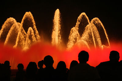 Silhouette people watching fountain against sky at night