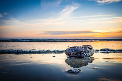 Rocks on beach against sky during sunset