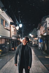 Young man looking up standing amidst building at night