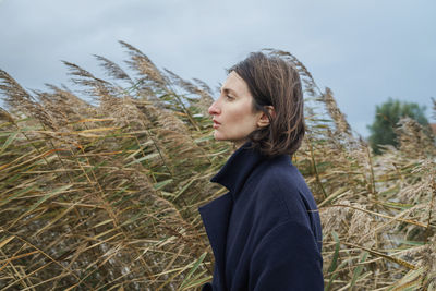 Side view of young woman standing on field against sky