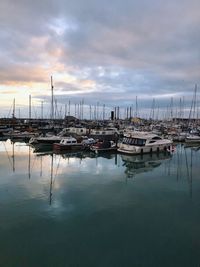 Sailboats moored in harbor at sunset