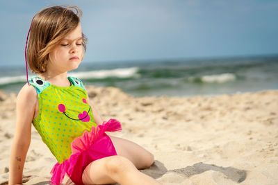 Girl relaxing on sand at beach against sky