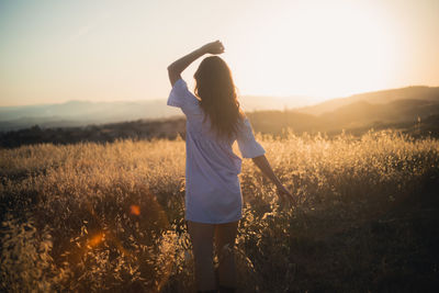 Rear view of woman standing on field against sky during sunset