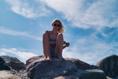 Woman sitting on rock against sky