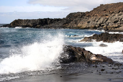 Waves splashing on rocks at shore against sky