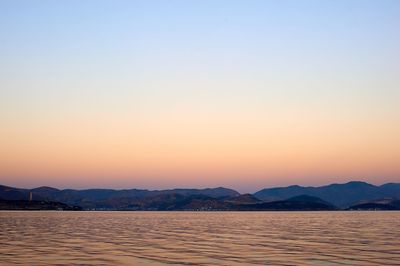 Scenic view of lake by mountains against clear sky during sunset