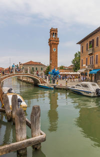 View of boats in canal by buildings against sky