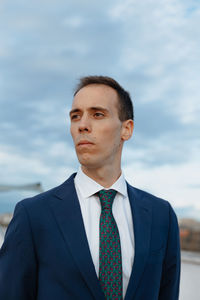 Young businessman in a suit and tie looking away thoughtful outside with a cloudy sky