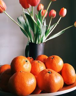 Close-up of oranges in plate with tulips in vase