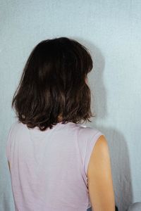 Rear view of woman sitting against white wall