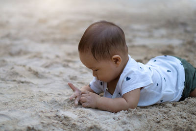 Cute baby boy lying on sand at playground