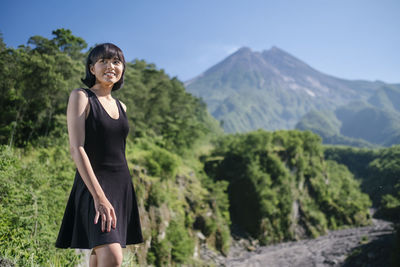 Smiling young woman standing on land against mountains and sky
