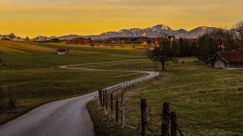 Road by agricultural field against sky during sunset