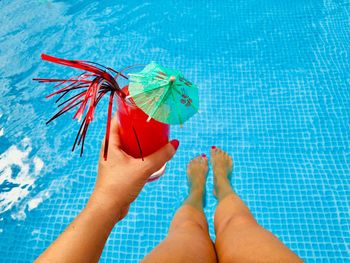 Low section of woman holding drink while sitting by swimming pool