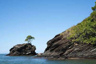 Rock formations by sea against clear blue sky