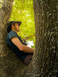 Side view of man climbing on tree trunk in forest