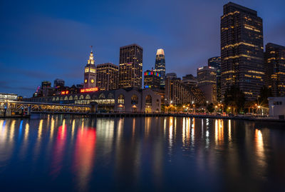 Illuminated buildings by river against sky at night