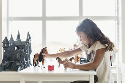 Side view of girl playing with toy horses at table