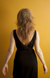 Rear view of young woman standing against yellow background