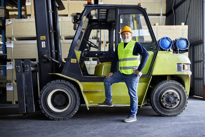 Portrait of confident mature worker at forklift in factory