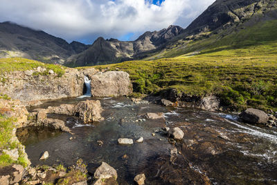 Scenic view of stream by mountains against sky