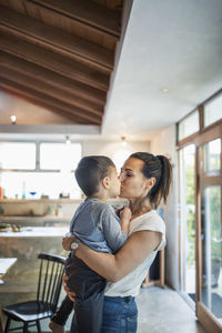 Affectionate woman kissing son at home