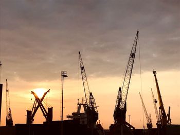 Silhouette cranes at commercial dock against sky during sunset