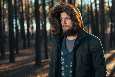 Young man standing by trees in forest