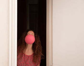 Young woman blowing balloon while standing by wall