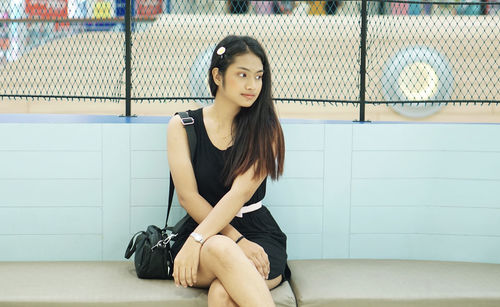 Beautiful young woman sitting against wall