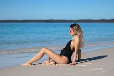 Portrait of young woman in black bikini and brown sunglasses sitting on beach in eastern australia
