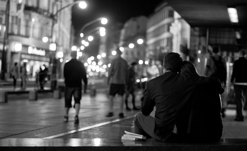 Rear view of people sitting on illuminated street at night