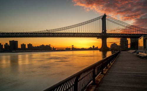 Manhattan bridge over east river against sky during sunrise seen from brooklyn park