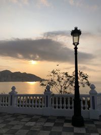 Street light by sea against sky during sunset