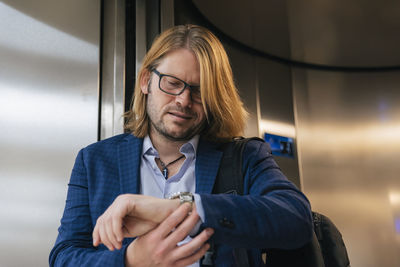 Businessman checking time on wristwatch at elevator