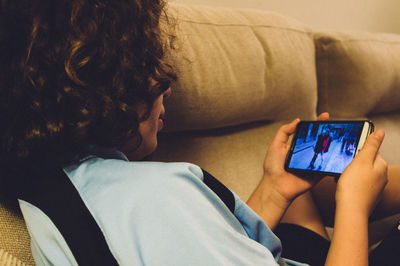 Girl watching photographs in mobile phone while reclining on sofa at home