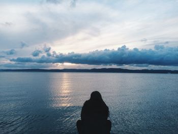 Rear view of silhouette woman crouching by lake against sky during sunset