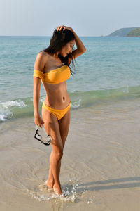 Young woman wearing bikini standing at beach against clear sky