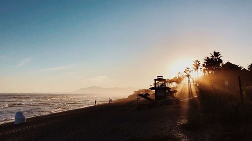 Scenic view of people on beach against sky during sunset