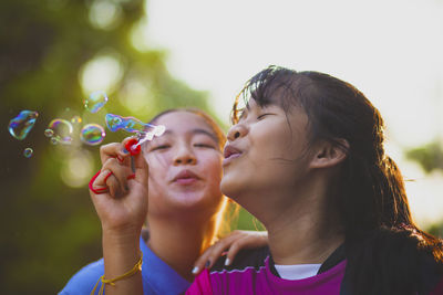 Close-up of girls bowing bubbles outdoors