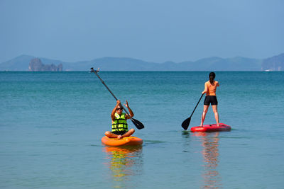 Asian senior father playing paddle board with young daughter at blue sea on summer vacation