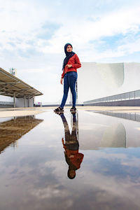 Full length of woman standing by puddle against sky