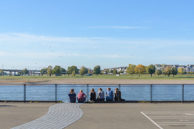 Group of people sitting on outer railing side along riverside of rhine river in düsseldorf, germany.