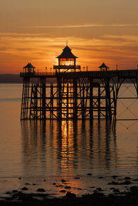 Silhouette built structure by sea against orange sky