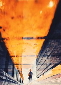 Man walking on bridge against sky during sunset