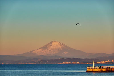 Scenic view of sea against sky and snow covered mountain during sunrise