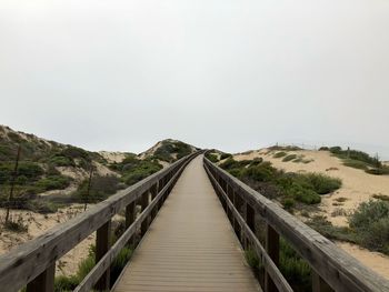 Wooden footbridge leading towards plants against clear sky