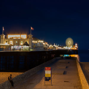 Illuminated city by river against clear sky at night