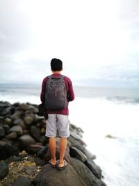 Rear view of man with backpack looking at sea while standing on rock