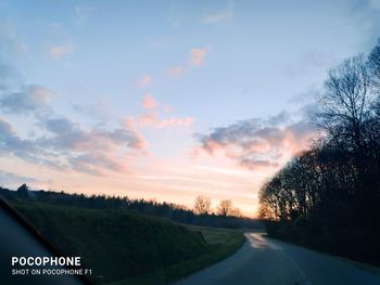 Road by trees against sky during sunset